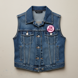 Button badge with 'Pink Out' text and bow design on a jean vest.