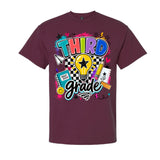 A maroon short-sleeve crewneck t-shirt featuring a colorful 'Third Grade' graphic on the front, complete with a lightbulb, checkered pattern, and school-themed doodles, shown against a plain white background.