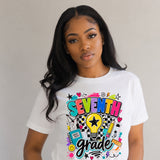 A woman wearing a white short-sleeve graphic T-shirt with colorful text reading 'SEVENTH grade' and school-themed doodles, photographed against a plain light gray background.