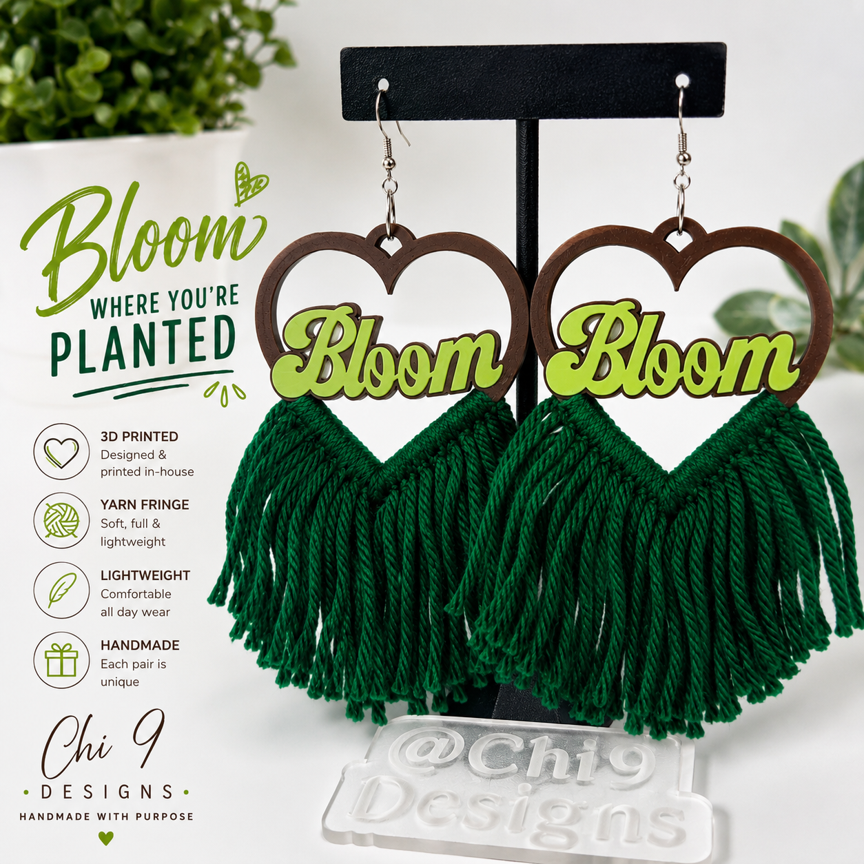 A pair of handmade tassel earrings displayed on a black stand, featuring brown heart-shaped wooden tops with lime green 'Bloom' lettering and dark green yarn fringe tassels. The image includes product features text on the left and a clear brand nameplate at the bottom.