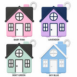 Four small house-shaped keychains shown in a 2x2 grid on a white background, labeled Baby Pink, Lavender, Mint Green, and Sky Blue. Each keychain has a house design with windows, a door, a roof, a small bag loop, and a small key ring.