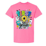 A bright pink short-sleeve t-shirt with a colorful graphic on the front that reads 'FIRST grade' surrounded by school-themed doodles like a lightbulb, notebook, pencil, and stars, shown on a plain white background.