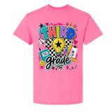A bright pink short-sleeve t-shirt with a colorful retro-style graphic on the front reading 'THIRD grade' in bold multicolored letters, surrounded by school-themed doodles like a lightbulb, notebook, pencil, and stars.