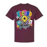 A maroon short-sleeve crewneck t-shirt featuring a colorful graphic on the front that reads 'SECOND grade' with school-themed doodles including a lightbulb, notebook, pencil, and stars.
