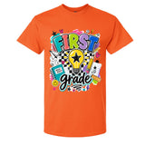An orange short-sleeve crewneck t-shirt featuring a colorful 'FIRST grade' graphic on the front, complete with a lightbulb, stars, hearts, and school supplies, shown against a plain white background.