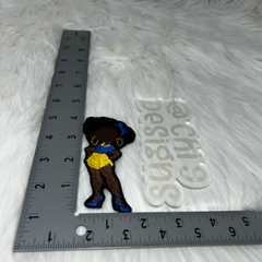 A close-up view of an embroidered patch featuring an African American woman in a retro pin-up style, with a blue and yellow outfit, displayed next to a ruler for scale on a white fur background. The image includes the text 'Choose Your Size' and mentions two available sizes: 4x2 inches or 7x3.5 inches. Chi 9 Designs branding is displayed at the top left corner with website links at the bottom.