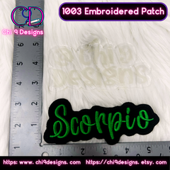 A close-up view of a 'Scorpio' embroidered patch in green thread with a black border, displayed next to a ruler on a white fur background for scale. The text '1003 Embroidered Patch' and 'Chi 9 Designs' branding are shown at the top with the website links at the bottom.