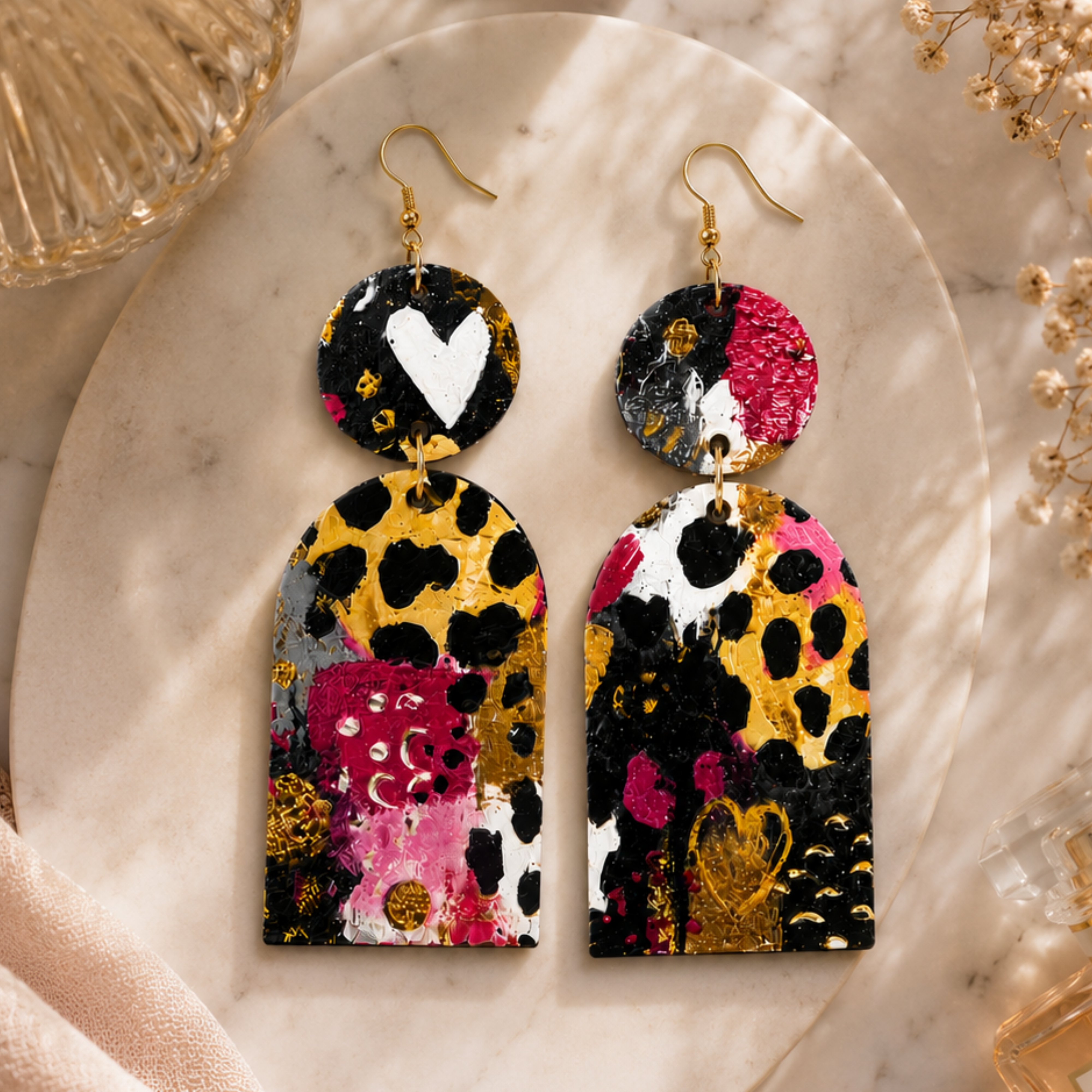 Handmade wood statement earrings with colorful abstract artwork styled on a marble surface with luxury accessories.
