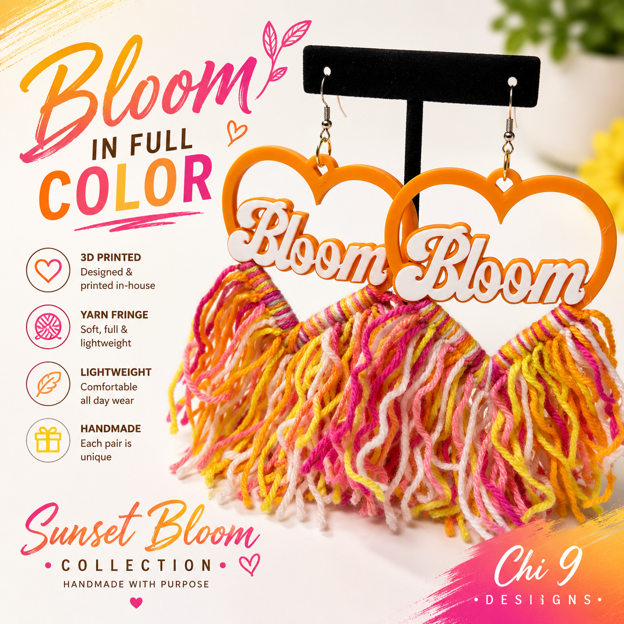 A pair of handmade heart-shaped dangle earrings displayed on a black stand. The earrings feature orange heart-shaped tops with white cutouts containing the word 'Bloom' in script, and fluffy fringe below in orange, yellow, pink, and white yarn.