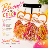 A pair of handmade heart-shaped dangle earrings displayed on a black stand. The earrings feature orange heart-shaped tops with white cutouts containing the word 'Bloom' in script, and fluffy fringe below in orange, yellow, pink, and white yarn.