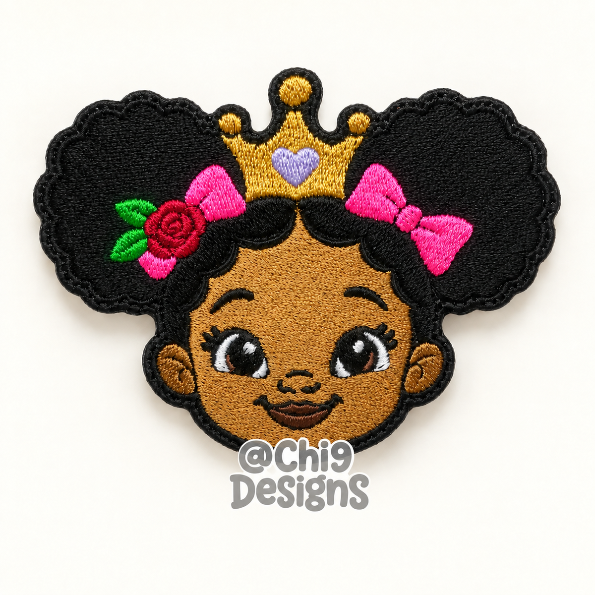 An embroidered patch featuring a cartoon girl with dark skin, black hair in pigtails, a gold crown, pink bows, and a red rose, shown on a plain white background with a watermark at the bottom.